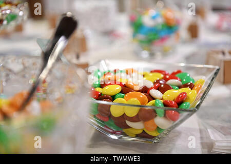 Glass bowl of brightly colored chocolate candies in the colors of the rainbow displayed on a table with selective focus Stock Photo