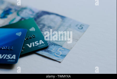 LONDON, UK, MAY 2019 Two debit cards, Barclays Bank and Lloyds and a 5 pound note. Woman's hand is holding Barclays Card, Tesco Club Card in the backg Stock Photo
