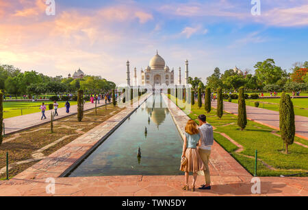 Taj Mahal white marble mausoleum at sunset with view of tourist couple enjoying the view at Agra, India Stock Photo