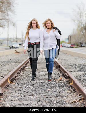 Mother and daughter standing and walking on the train tracks in an urban setting. Stock Photo