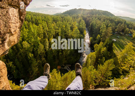 Climber's legs hanging on a rope in a harness, first person view to river in forest Stock Photo