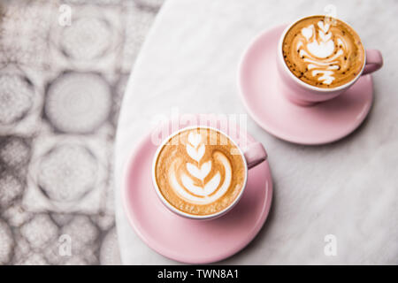 Two pink cups of cappuccino with beautiful latte art on marble table background. Top view. Stock Photo