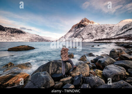 Seascape with snow mountain and photographer standing on rock at coastline, Segla, Northern Norway Stock Photo