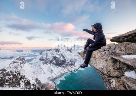 Mountaineer sitting on rock at the peak mountain of arctic coastline at sunset. Ryten Mountain, Lofoten islands, Norway Stock Photo