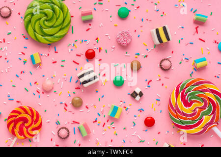 flat lay of festive background with assortment of colourful caramel candies with jelly and sprinkles over pink Stock Photo