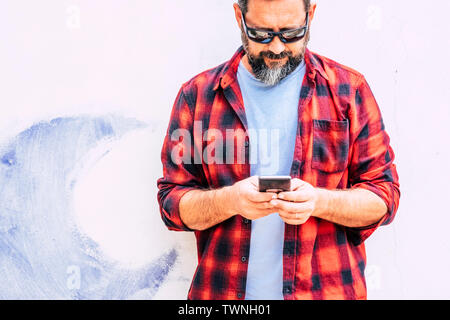 Coloured hipster people adult man with beard usgin modern cellular smart phone - standing on a white wall background - alternative job and work office Stock Photo