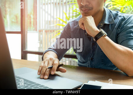 Man working on laptop with cell phone on wooden desk. Stock Photo