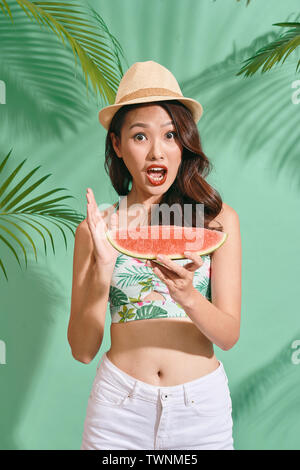 Slice of summer goodness. Beautiful young woman holding slice of watermelon and smiling while standing on blue background Stock Photo