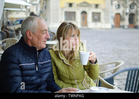 Middle-aged woman and her elderly husband spending time together outdoors sitting in cafe with terrace outdoors and drinking coffee in the morning Stock Photo