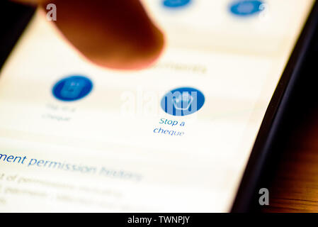 Stop a cheque button on smartphone app screen closeup with human finger pointing to it Stock Photo