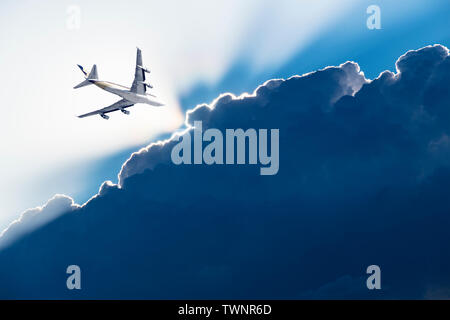 line airplane crosses the stormy sky, half of the diagonal sky is dark blue, the other half is white and illuminated by the rays of the sun Stock Photo