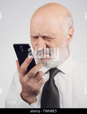 Senior man using apps on the smartphone, he is having difficulties and vision problems Stock Photo