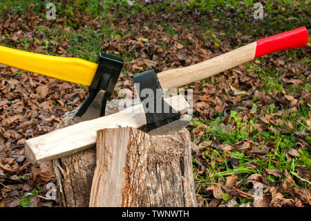 Two axes with steel blades stuck in old stump on autumn dry leaves background Stock Photo