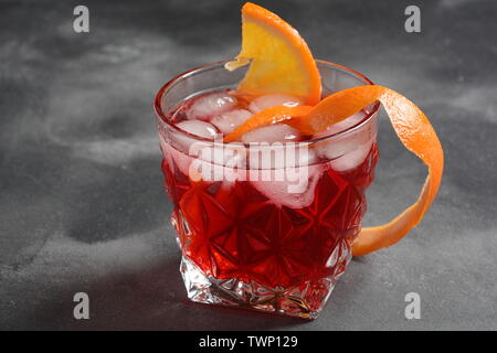 Negroni cocktail. Smoky Italian aperitif with gin, campari, martini Rosso, orange and ice cubes served in glass on dark stone background Stock Photo