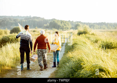 Young man and woman walking on the picnic with senior grandfather dressed in sweaters, spending a good time together on the nature Stock Photo