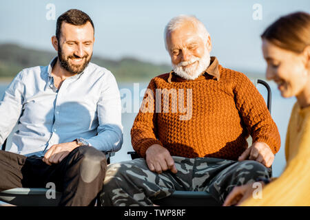 Man and woman having warm conversation with senior grandfather during the picnic near the lake in the morning Stock Photo