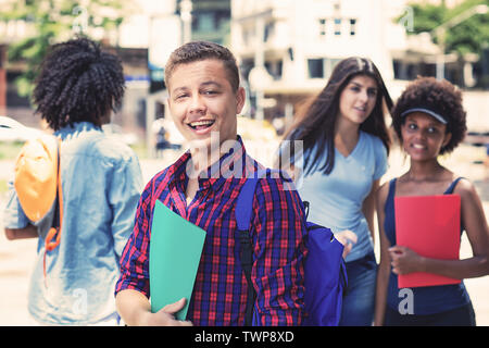 Handsome brazilian male student with group of students outdoors in city in summer Stock Photo
