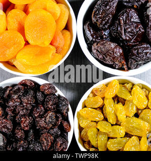 Selection of Healthy Dried Fruits Soft Apricots, Prunes, Raisins and Sultanas in White Bowls Looking Down With No People Stock Photo