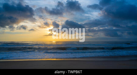 A wide-angle shot that captures the golden glow of the early morning sun breaking through the clouds and reflected in waters of the Atlantic Ocean. Stock Photo
