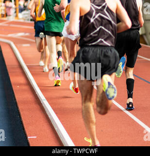 Looking at a group of high school track runners on an indoor track from behind during a mile race. Stock Photo