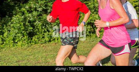 Three high school girls are running together on a grass field in a local park during cross country practice. Stock Photo