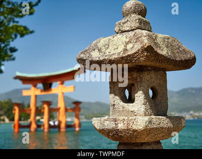 A stone lantern in focus in front of a blurred Itsukushima torii. Stock Photo