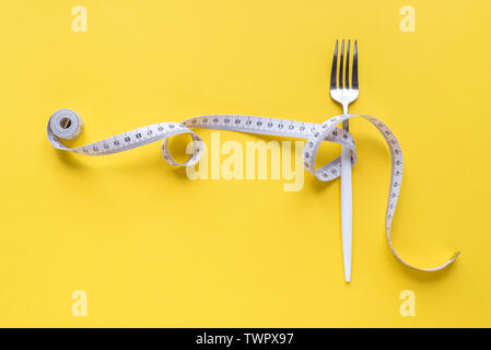 Fork and Measuring Tape on yellow background, copy space. Diet, healthy lifestyle, weight loss concept with white fork and measuring tape. Stock Photo