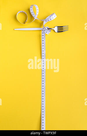 Fork and Measuring Tape on yellow background, copy space. Diet, healthy lifestyle, weight loss concept with white fork and measuring tape.