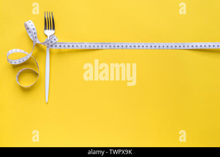 Fork and Measuring Tape on yellow background, copy space. Diet, healthy lifestyle, weight loss concept with white fork and measuring tape. Stock Photo