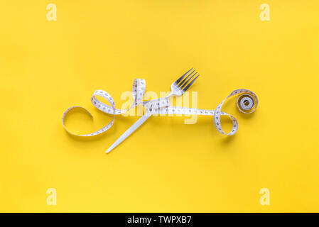 Fork and Measuring Tape on yellow background, copy space. Diet, healthy lifestyle, weight loss concept with white fork and measuring tape. Stock Photo