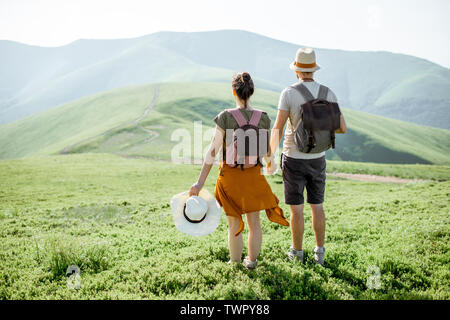 Young couple standing together with backpacks, enjoying beautiful view on the green mountains, rear view Stock Photo