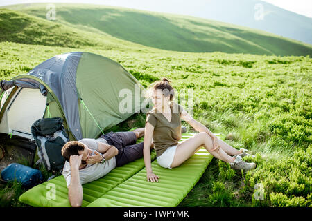 Young and cheerful couple lying on the mattress at the campsite, enjoying summer time while traveling in the mountains Stock Photo