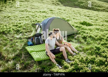 Young lovely couple sitting together on the mattress at the campsite, enjoying summer time while traveling in the mountains Stock Photo