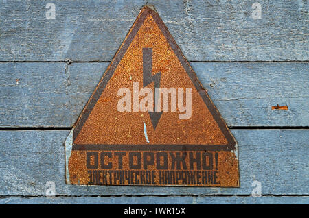 Old electrical safety warning signs on an abandoned military facility of the former USSR. Inscription - Caution! Electrical voltage Stock Photo