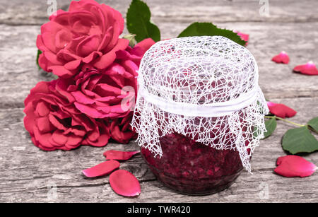 Jar of jam of rose petals on a wooden table with flowers of roses. Flower confiture. Healthy food. Copy space Stock Photo