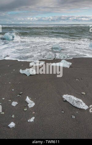 Waves crushing onto icebergs and ice floes on the black sandy beach at Diamond beach, Iceland. Stock Photo