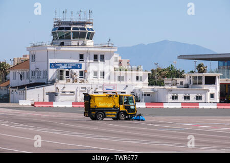 Gibraltar International Airport with Control Tower and airport vehicle sweeping runway crossed by the main road. Stock Photo