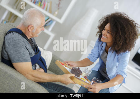 carer bringing meal to elderly man with arm injury Stock Photo