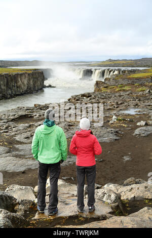 Hikers looking at Iceland nature by waterfall Selfoss waterfall. People enjoying view of famous Icelandic tourist attraction. Hiking couple taking break by Selfoss in Vatnajokull national park. Stock Photo