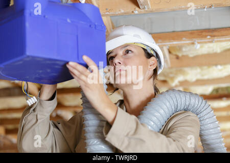 female worker fitting ventilation system in buildings ceiling Stock Photo