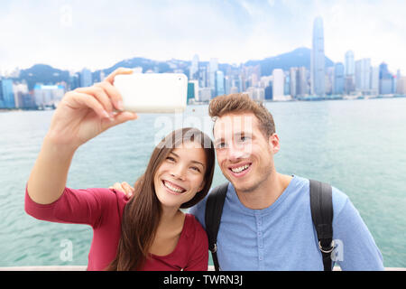 Selfie - friends taking self-portrait picture photo in Hong Kong enjoying sightseeing on Tsim Sha Tsui Promenade and Avenue of Stars in Victoria Harbour, Kowloon, Hong Kong. Travel concept. Stock Photo