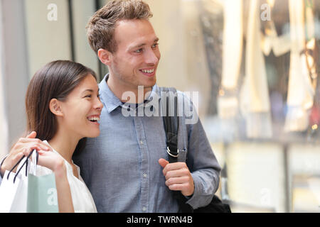 Couple shopping in Hong Kong Central looking at shop windows holding shopping bags. Urban mixed race Asian Chinese woman shopper and Caucasian man smiling happy living in city. Stock Photo
