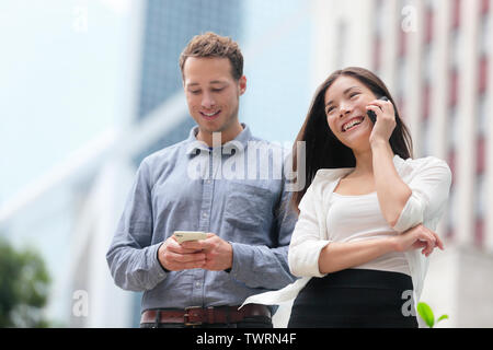 Young urban professionals business people on smartphones in Hong Kong. Businessman using app on smartphone and businesswoman talking having conversation on smart phone in Hong Kong Central. Stock Photo