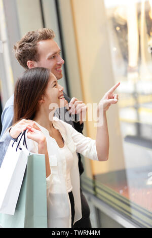 Woman and man shopping in Hong Kong Central. Couple looking at shop windows holding shopping bags. Urban mixed race Asian Chinese woman shopper and Caucasian man smiling happy living in city. Stock Photo