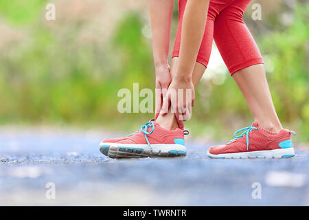 Twisted broken ankle - running sport injury. Female runner touching foot in pain due to sprained ankle.