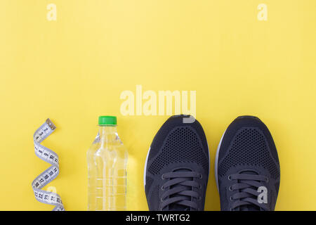 Fitness flat lay. Healthy lifestyle and sport concept. Black sneakers, tape measure and bottle of water on a yellow background. Stock Photo