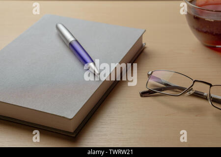 Eyeglasses, diary, blue pen and cup of tea on a brown table, selective focus. Stock Photo