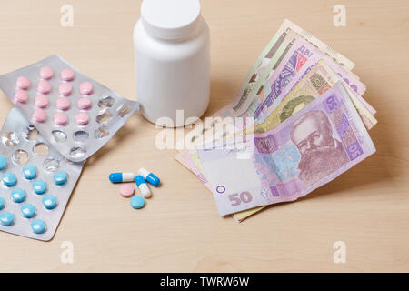 Medicines, blue and pink pills and Ukrainian money on the table. Stock Photo