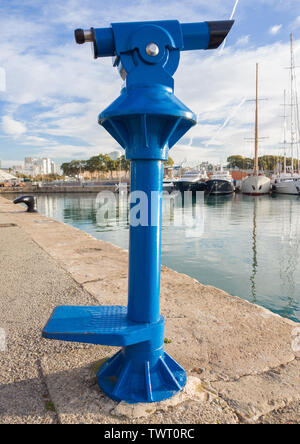 Blue tourist monocular for sightseeing on the background of yachts standing in the marina of the seaside town. Stock Photo