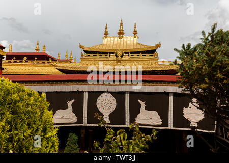 View of the golden colored rooftop of Jokhang Temple. The famous dharma wheel with deers can be seen on the roof  and on the banner in the front.